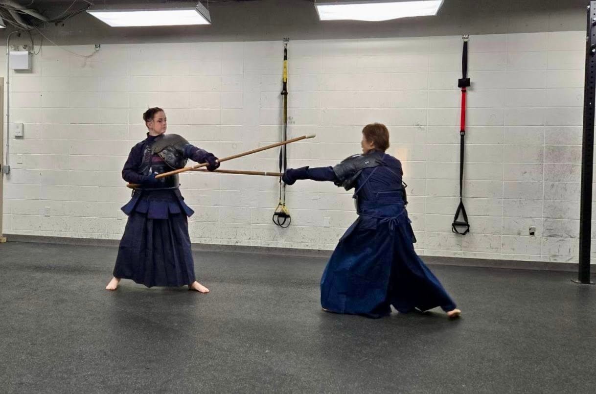 Two jūkendō practitioners in protective armour practice a thrust and defence with wooden training rifles.